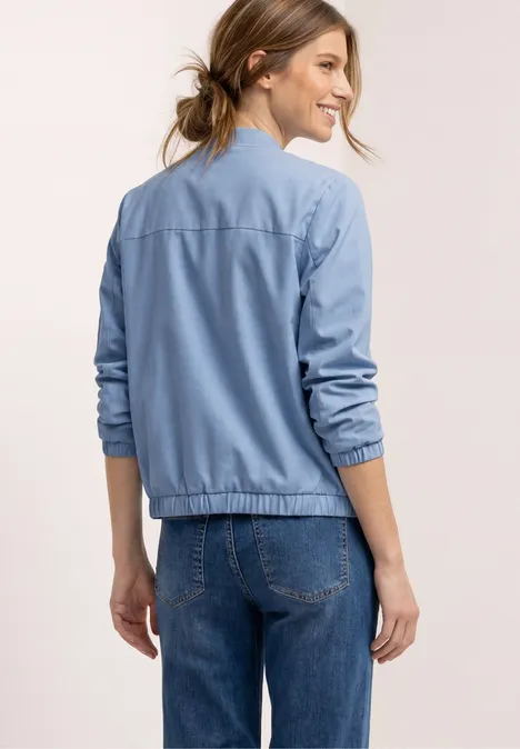 Vrouw van achteren in een blauwe bomberjas en spijkerbroek.