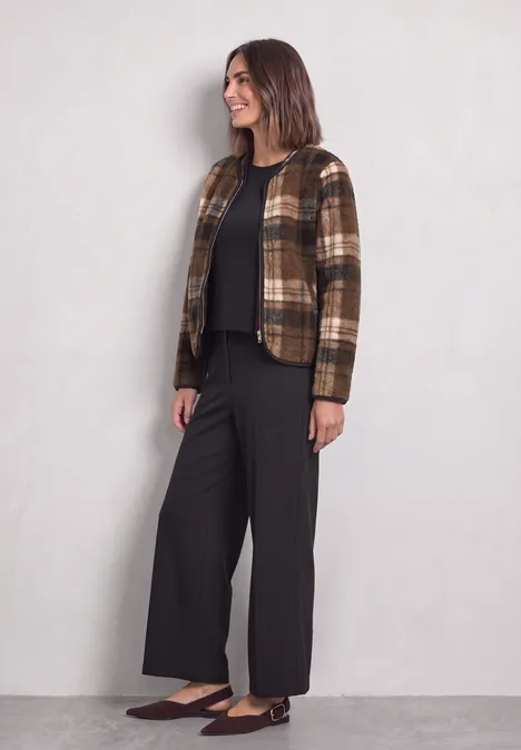 Teddy-Jacke mit Rundhals und Print Obsidian Blue Frau trägt schicke braun-kariert Jacke, schwarzen Pullover, weite schwarze Hose und flache braune Schuhe.