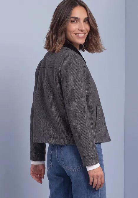 Frau mit grauer Jacke und Jeans, im Rücken fotografiert, blickt lächelnd über die Schulter
