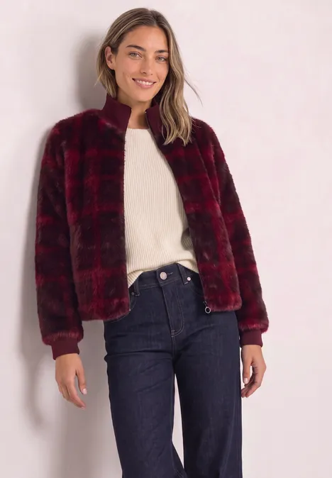 Blouson en fausse fourrure avec des détails en maille et un imprimé plummy brown Frau trägt rotschwarz karierte, flauschige Jacke mit Reißverschluss über weißem Pullover und Jeans.