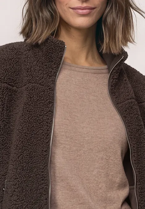 Osoba ma na sobie brązową kurtkę teddy fleece na beżowym topie.