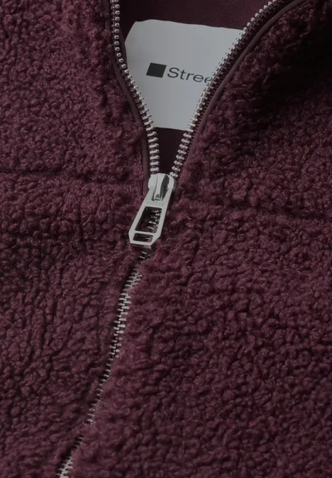 Zbliżenie bordowej polarkowej bluzy z metalowym zamkiem i widoczną metką.