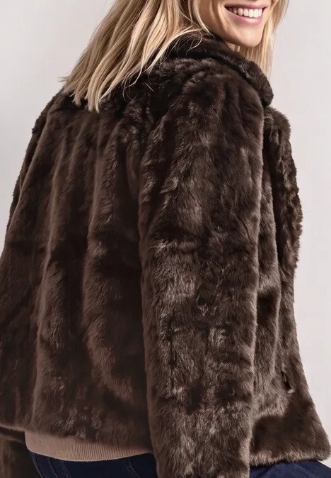 Kurze Fake-Fur-Mix Jacke mit Kapuze auburn brown Teilausschnitt einer Frau mit blondem Haar, die einen braunen Kunstpelzmantel trägt und lächelt.
