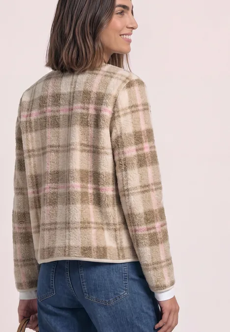 Eine Frau von hinten in einem beige karierten Blazer mit rosa Streifen, kombiniert mit blauen Jeans.