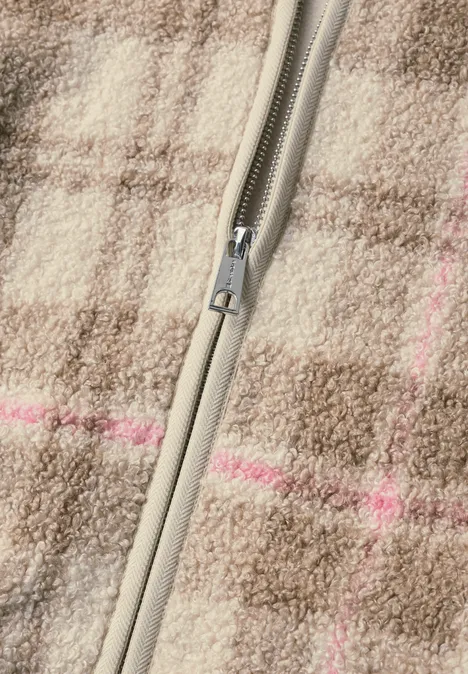 Nahaufnahme eines graubeigen Reißverschlusses auf kariertem Wollstoff in Braun mit dezenten rosa Streifen.