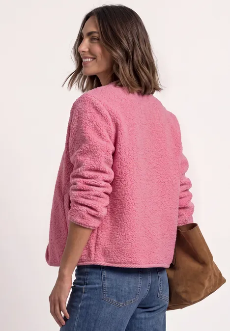 Frau trägt pinke Teddyjacke, blickt über die Schulter, kombiniert mit Jeans und einer braunen Tasche.