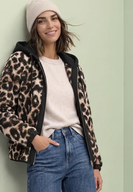 Teddy-Blouson mit abnehmbarer Kapuze Black Frau in Jeans, Beanie und Leoparden-Fleecejacke lächelt entspannt.