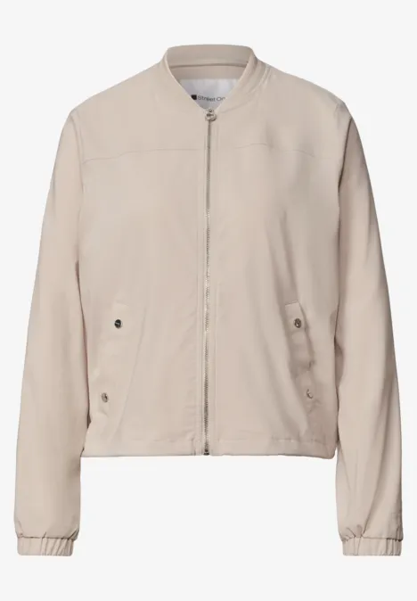 Helles beiges Bomberjacke mit Reißverschluss, seitlichen Taschen und langen Ärmeln.