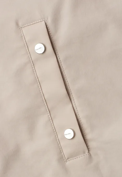 Detailaufnahme eines hellbeigen Stoffteils mit zwei silbernen Druckknöpfen an einer rechteckigen Klappe.