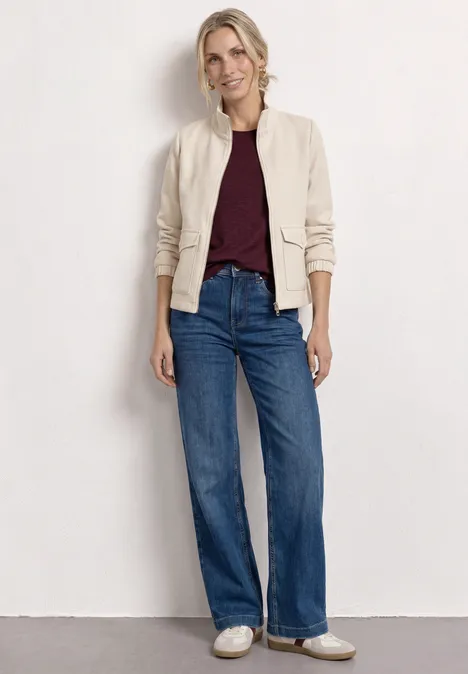 Femme en bomber beige, haut bordeaux, jean large taille haute et baskets blanches.
