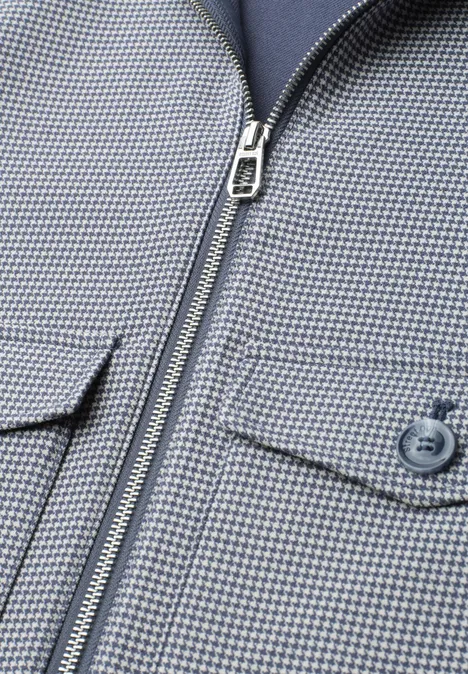 Gros plan d'une veste gris clair à motif micro-carreaux bleus, fermeture éclair et poche à bouton