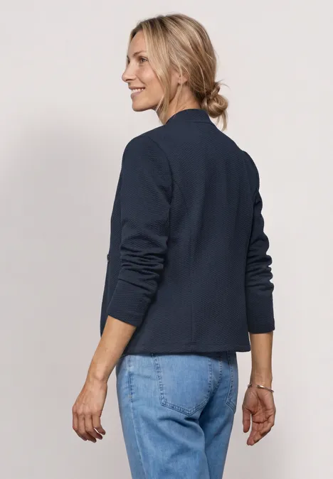 Une femme de profil porte une veste bleu marine et un jean, visage flou et cheveux noués.