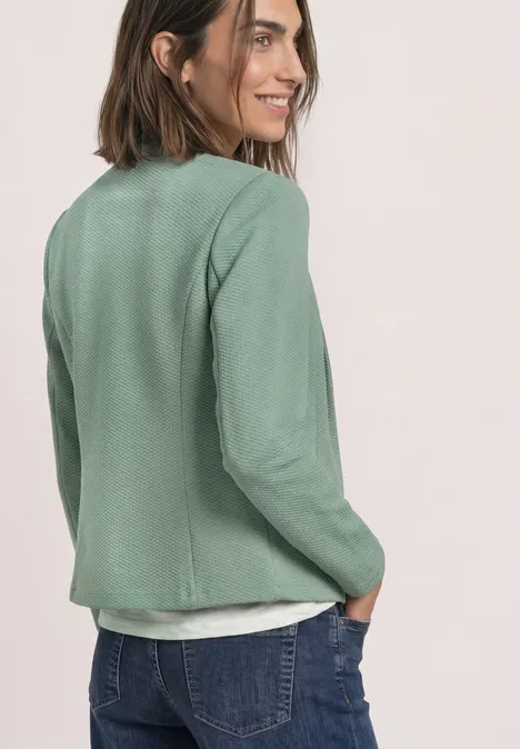 Blazer mit Reverskragen und Struktur eucalyptus green Frau im grünen Blazer und Jeans, lächelt zur Seite und hat Hände in den Hosentaschen.