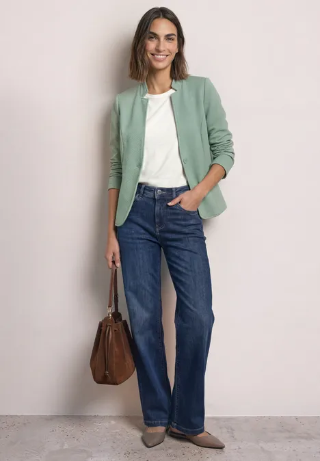 Blazer mit Reverskragen und Struktur eucalyptus green Frau trägt grünen Blazer, weiße Bluse, blaue Jeans und hält eine braune Tasche.