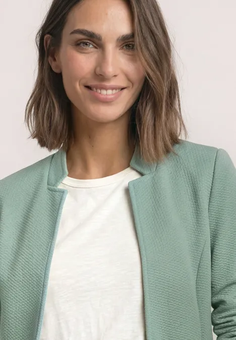 Blazer mit Reverskragen und Struktur eucalyptus green Eine lächelnde Frau mit schulterlangen braunen Haaren trägt ein weißes T-Shirt und eine hellgrüne Strickjacke.