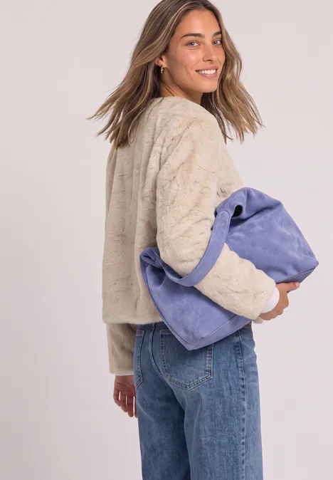 Frau in beiger Jacke trägt große blaue Handtasche und lächelt über die Schulter.