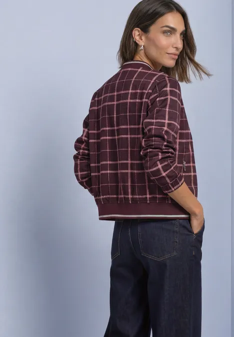 Frau trägt karierte Bomberjacke und Jeans, Blick über die Schulter, Rückansicht.