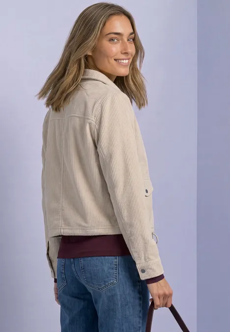 Lächelnde Frau im beigen Blouson und Jeans mit Tasche, Blick über die Schulter.