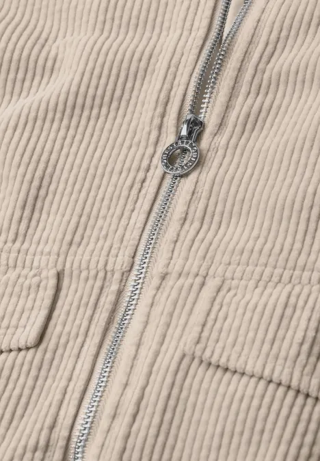 Beige Cordjacke mit sichtbarem Reißverschluss und rundem Metall-Zippergriff.