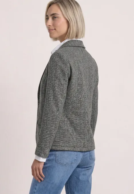 Seitlich zu sehen: Frau in grauem Blazer, weißer Bluse und blauen Jeans.