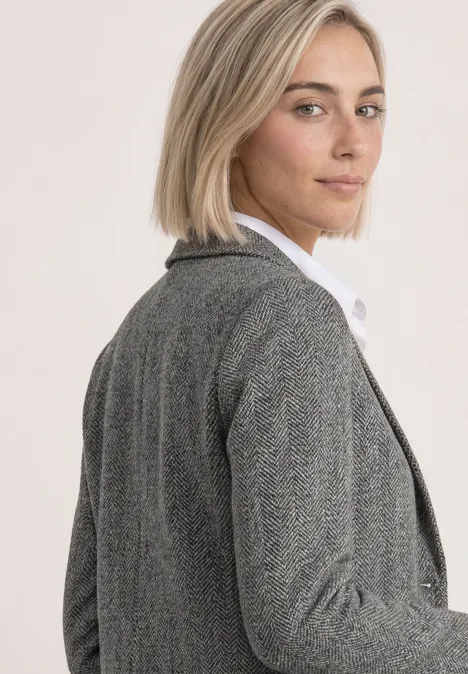 Eine blonde Frau im grauen Blazer und weißem Hemd schaut über die Schulter.