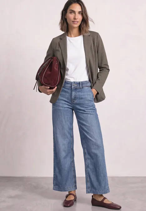 Frau in weißem T-Shirt, olivgrünem Blazer und weitem Jeans, mit weinroter Handtasche und Loafers.