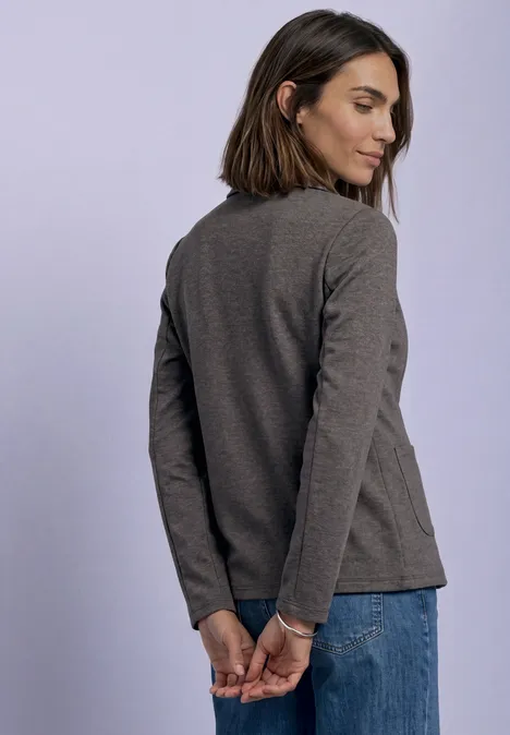 Junge Frau von hinten in grauem Langarmshirt und Jeans, Hände hinter dem Rücken verschränkt.