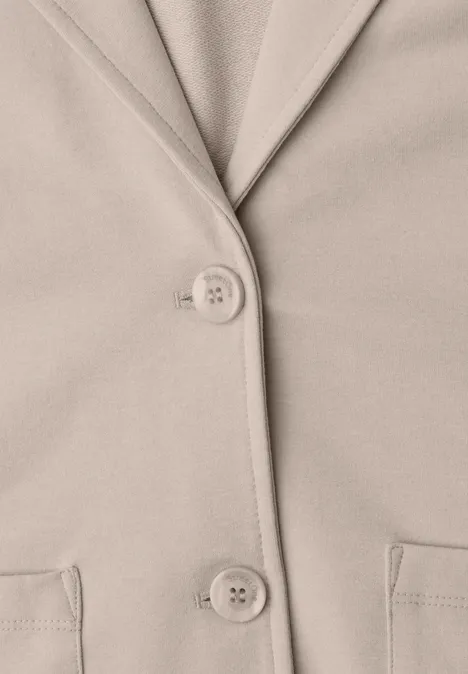 Beige Jacke mit Reverskragen, zwei Knöpfen und zwei aufgesetzten Taschen.