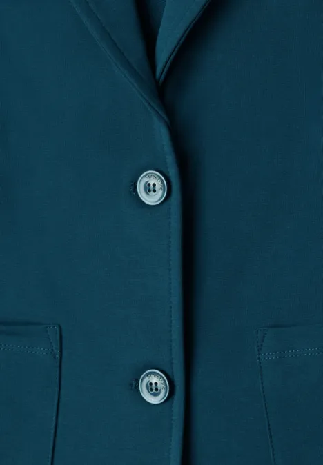 Nahaufnahme eines petrolfarbenen Blazers mit zwei Knöpfen und aufgesetzten Taschen.
