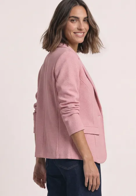 Frau in rosa Blazer und Jeans lächelt seitlich in die Kamera.