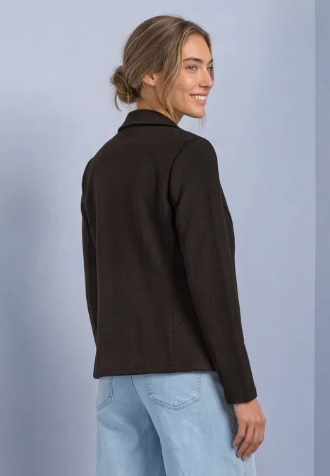 Femme en veste noire et jean, de profil, regarde par-dessus l’épaule et sourit.