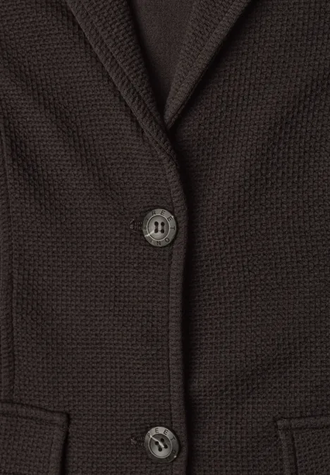 Gros plan d’un gilet marron en maille avec deux boutons et poches avant.