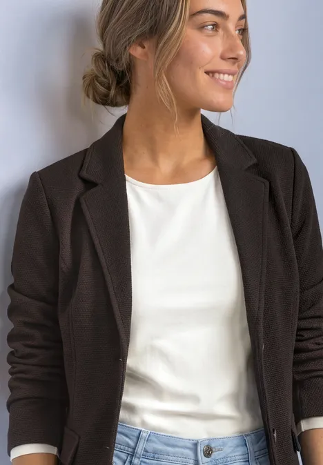 Une femme en blazer noir et haut blanc sourit de profil.