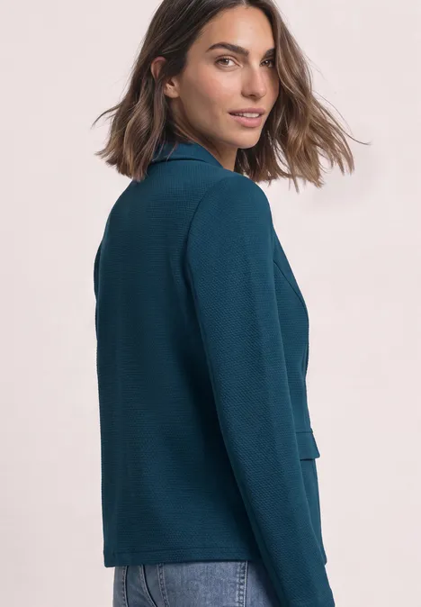 Frau in einem teal-blauen Blazer blickt seitlich über die Schulter.