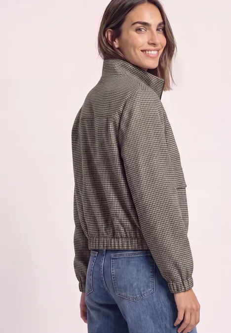 Vue arrière d’une femme souriante en veste gris-vert et jean sur fond clair