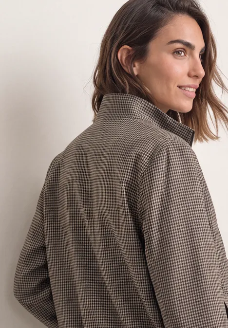 Femme aux cheveux mi-longs portant un manteau à carreaux regarde par-dessus son épaule.