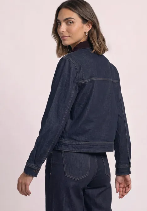 Femme portant une veste en jean sombre et un jean assorti, look sobre et tendance.