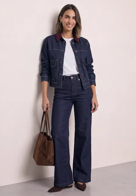Femme portant une veste en jean bleu foncé, un t-shirt blanc, un jean évasé et un sac à main marron.