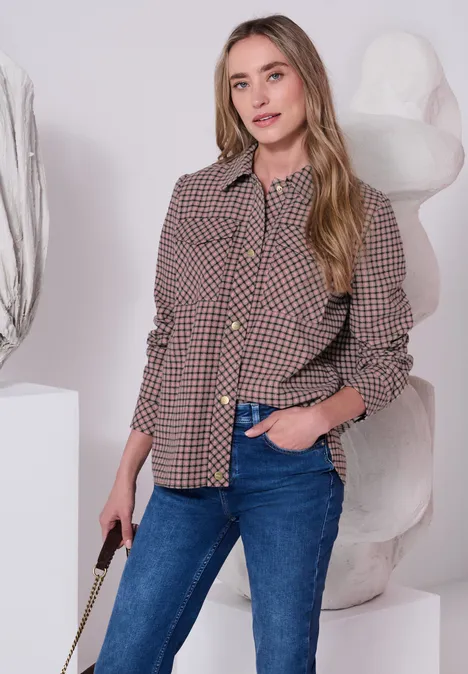 Overshirt z kieszeniami na piersi i wzorem w kratkę warm blush Młoda kobieta w kratowanej kurtce i dżinsach, uśmiechnięta, stoi przed rzeźbą trzymając torebkę.