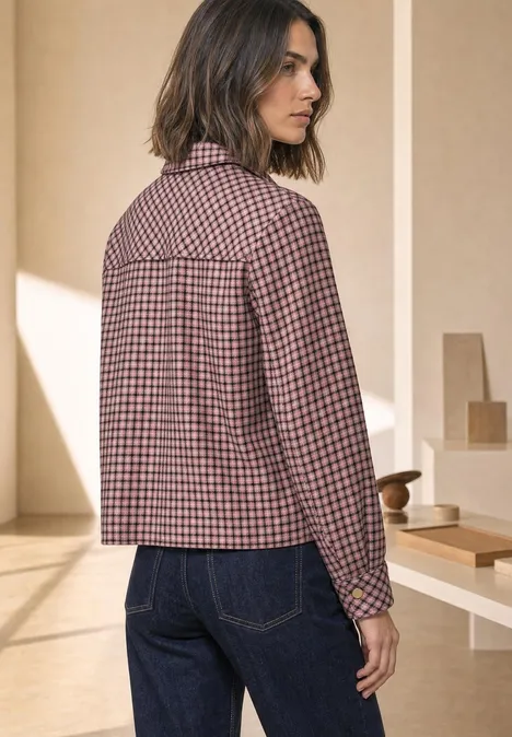 Overshirt z kieszeniami na piersi i wzorem w kratkę warm blush Kobieta z boku w kraciastej kurtce i dżinsach w jasnym wnętrzu.