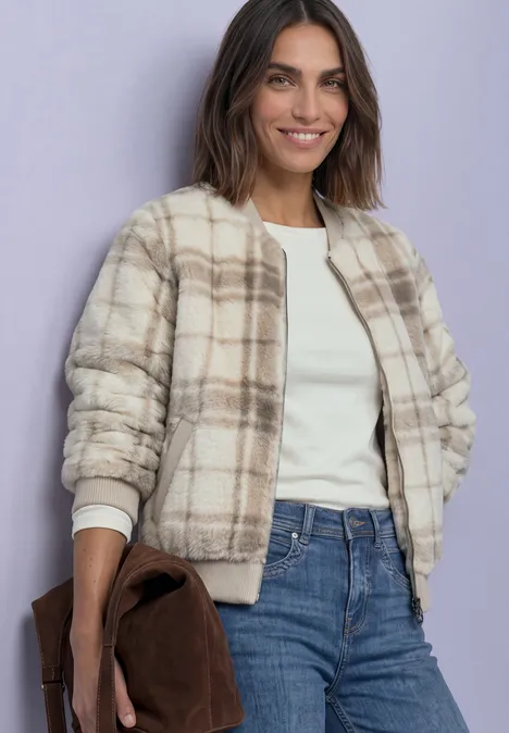 Femme porte une veste teddy à carreaux, chemise blanche, jean et sac marron.