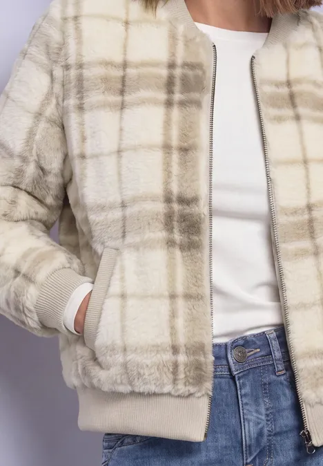 Buste d'une femme en veste crème à carreaux, T-shirt blanc et jean bleu.