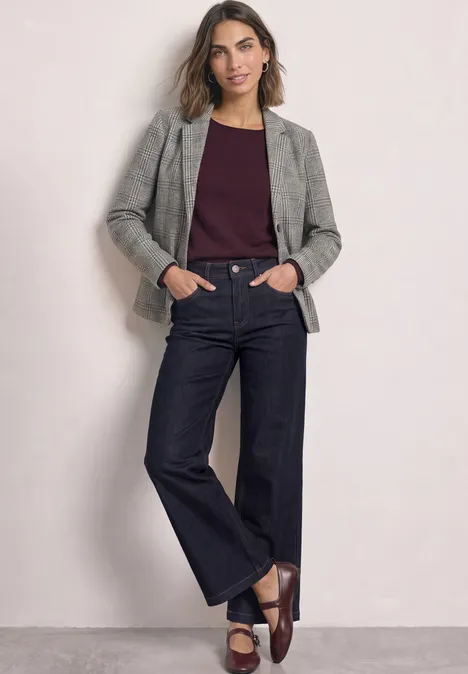 Blazer à carreaux et boutons Black Frau steht in grauem Blazer, dunkelrotem Top, weiten Jeans und braunen Slippern.