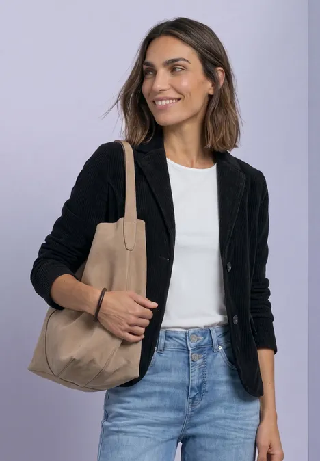 Frau mit schwarzem Blazer, weißem T-Shirt, Jeans und beiger Tasche lächelt.