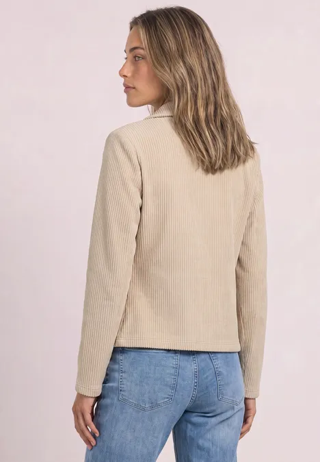 Frau steht im Profil, trägt eine hellbeige Jacke und blaue Jeans.