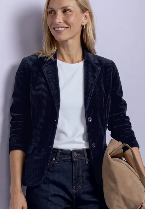 Frau in schwarzem Blazer, weißem Shirt und Jeans hält eine Tasche.