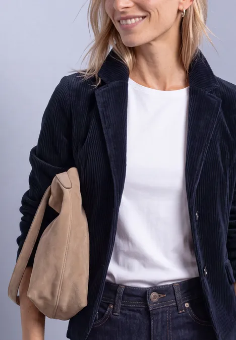 Frau mit weißem T-Shirt, dunklem Cord-Blazer und beiger Wildledertasche.