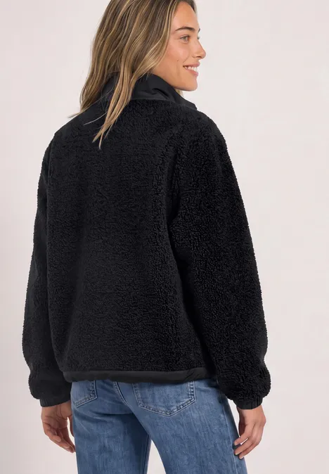 Frau trägt schwarzen, kuscheligen Teddy-Fleece-Pullover mit Stehkragen und halbem Reißverschluss.