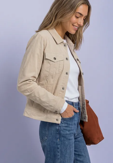 Seitliche Aufnahme einer lächelnden Frau mit beiger Jacke, weißem Shirt, Jeans und brauner Tasche.