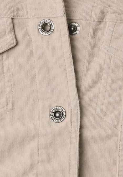 Nahaufnahme eines hellbeigen Cordjackenstoffs mit Metall-Druckknöpfen und aufgesetzter Tasche.